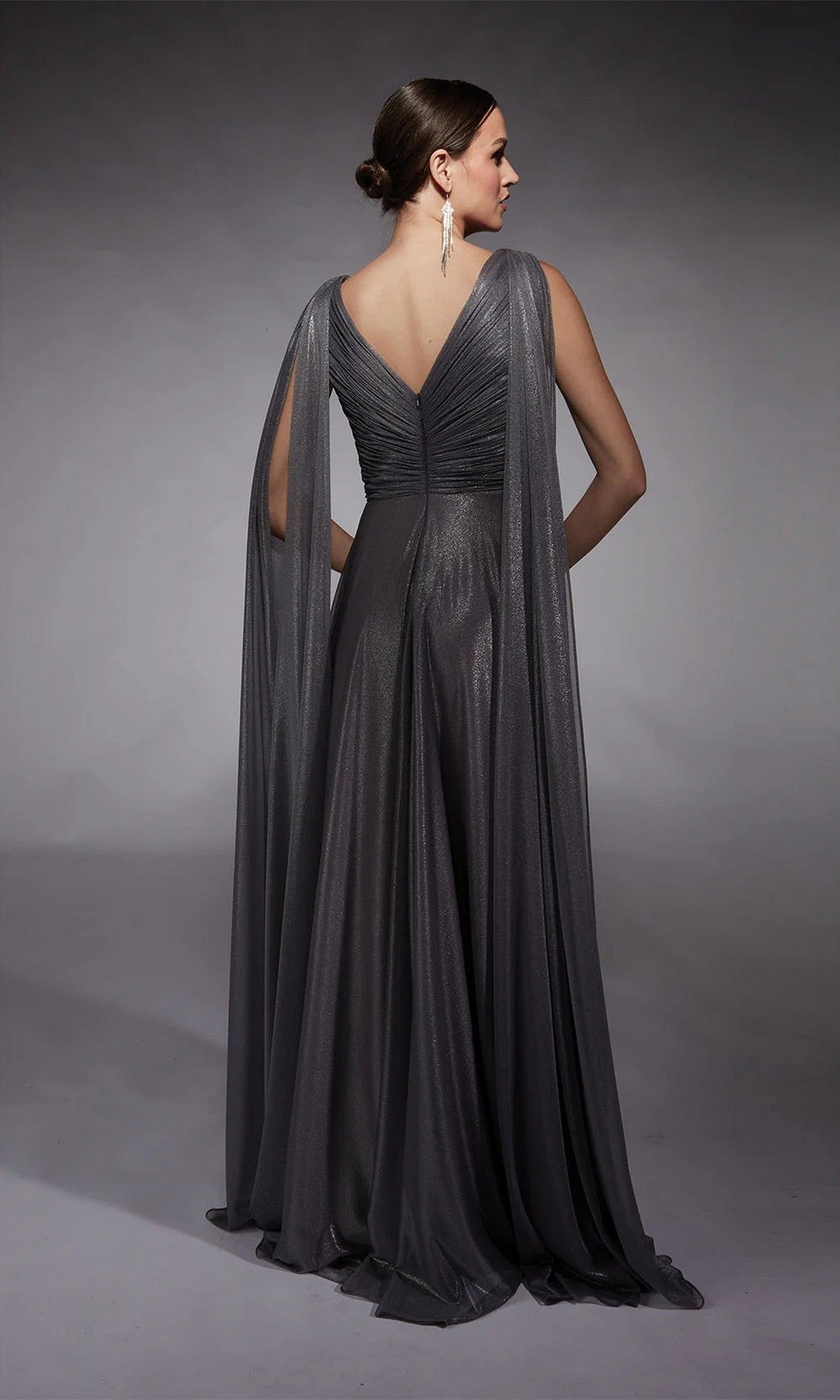 A woman faces away from the camera in the Alyce 27720, a floor-length metallic chiffon formal dress with draped cape sleeves and a V-back—an elegant choice for a sophisticated mother of the bride.