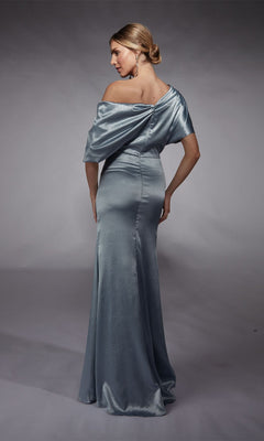 A woman models the Alyce 27721 Long Formal Dress—a silver, off-the-shoulder sheath gown—standing with her back turned and glancing over her shoulder against a plain gray backdrop.