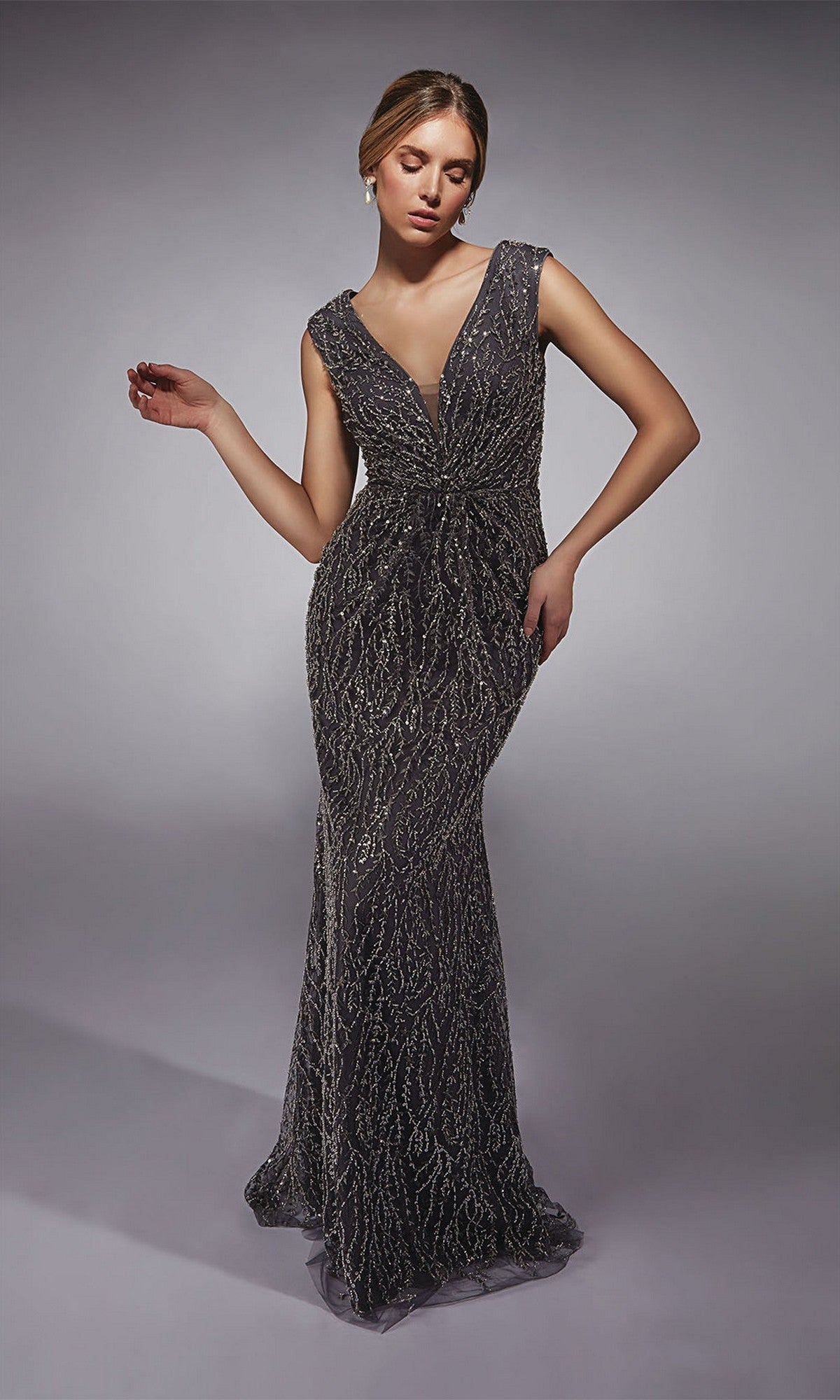 A woman stands against a plain background wearing the Alyce 27725 Long Formal Dress, a sleeveless, floor-length sequin evening gown with a fitted sheath silhouette and deep V-neckline.