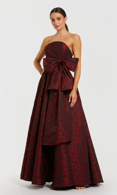 Woman wearing a burgundy strapless gown with a large bow on a white background