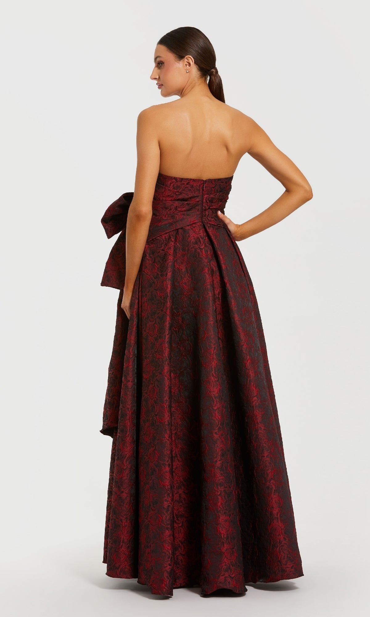 Woman wearing a burgundy strapless gown with floral pattern on a white background