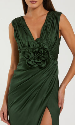 Wearing the Mac Duggal 27728 Long Formal Dress, she stuns in a sleeveless, deep green satin gown featuring a dramatic thigh-high slit and a large 3D floral applique accenting the waist.