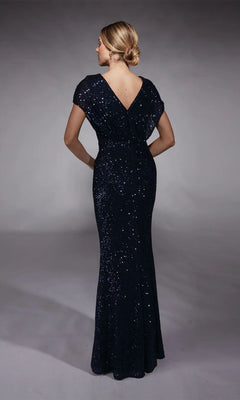 A woman with blonde hair in a low bun wears the Alyce 27729, a floor-length, short-sleeved dark blue sequin mother-of-the-bride gown with a V-back, standing against a plain background.