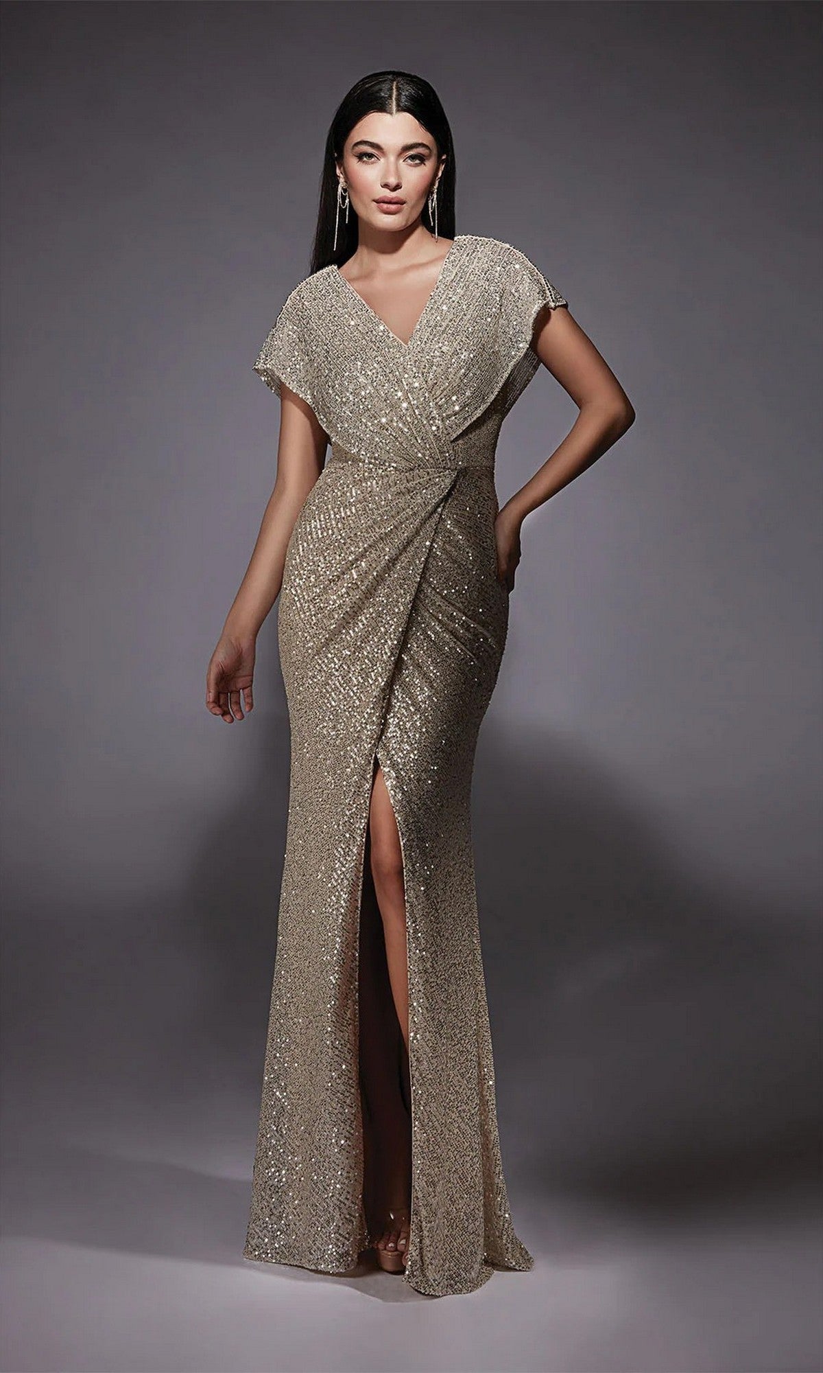 A woman wears the Alyce 27729 long formal dress in sand, featuring a floor-length design with short sleeves, V-neckline, wrap-style bodice, and front slit—an elegant choice for a mother-of-the-bride.