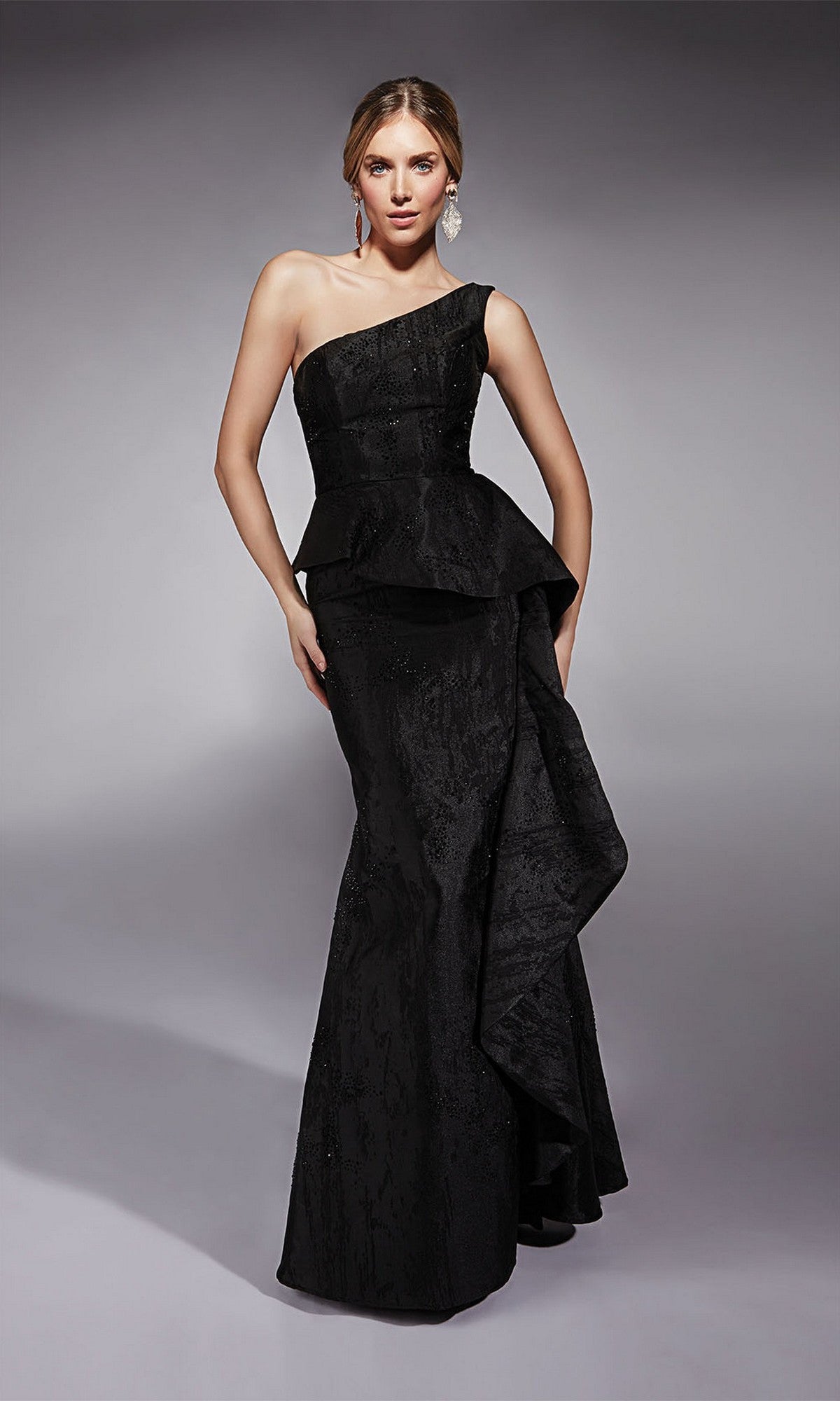A woman poses against a plain gray studio background in the Alyce 27732 long formal dress, a fitted black gown featuring an asymmetric peplum and side draping.