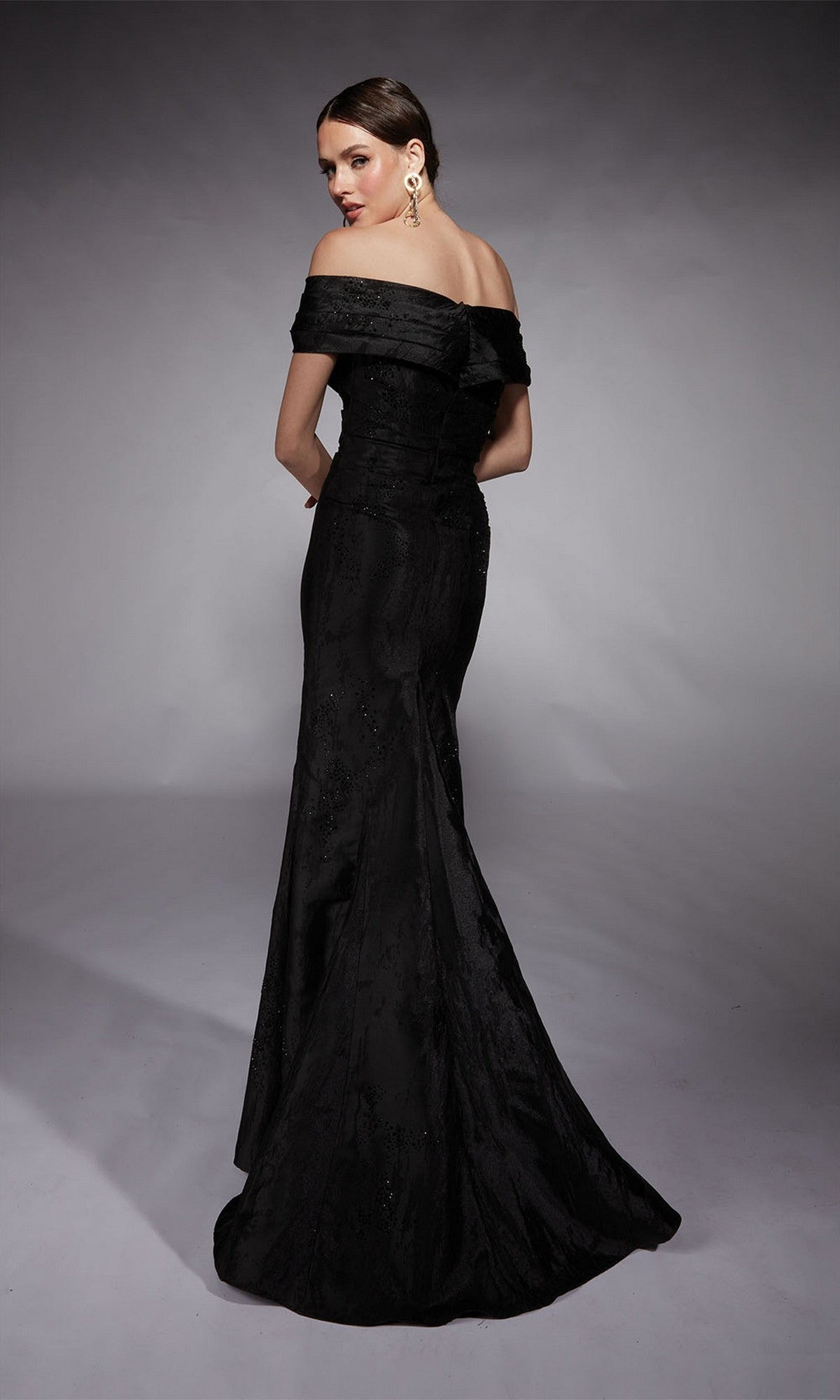 Woman wearing the Alyce 27733 long formal dress with a jacquard mermaid silhouette, posing with her back slightly turned against a plain gray background—ideal for elegant evening events.