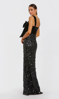 Model wearing the Mac Duggal 27738 long formal dress with a black velvet bodice, large shoulder bow, and sequined floor-length skirt, posed against a plain white background.