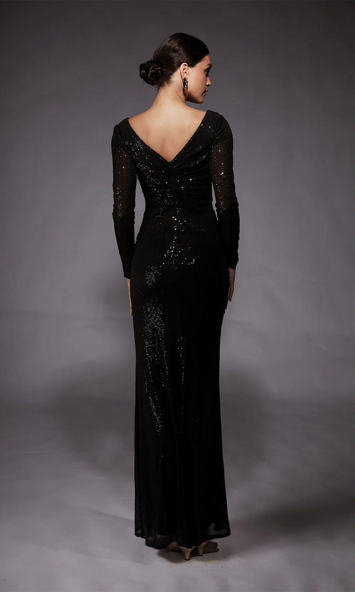 A woman faces away, wearing the Alyce 27741 long formal dress with a sequined design, deep V-back, and floor-length black sleeves, set against a neutral gray background.