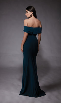 A woman stands facing away in the Long Formal Dress: Alyce 27745, highlighting the elegant back and side of the dark teal off-the-shoulder gown—perfect for prom—against a plain gray backdrop.
