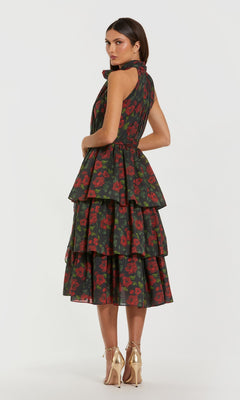 A woman models the Mac Duggal 27747 Midi Wedding Guest Dress, a sleeveless, tiered tea-length design with a red floral print on dark fabric, paired with gold heels and set against a plain white background.