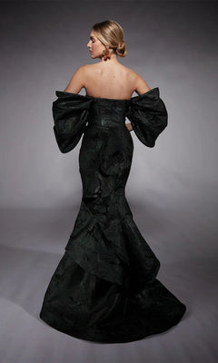 Wearing the Alyce 27747, a strapless forest green metallic jacquard corset dress with voluminous sleeves and a dramatic mermaid skirt, a woman stands in profile against a gray background.