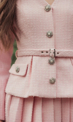Close-up of a person wearing the Mac Duggal 27752 Short Boucle Day Dress, featuring a pink textured fabric, embellished pearl buttons, a belted waist, and a pleated mini skirt.
