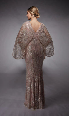 A woman with blonde hair in a low bun models the Alyce 27756 long formal dress, featuring floor-length geometric sequins and wide, sheer sleeves, as she stands with her back to the camera against a plain gray backdrop.