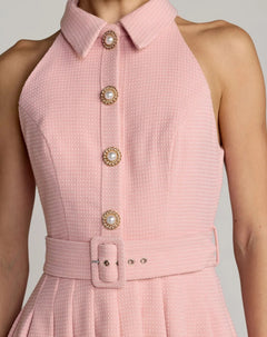 Wearing the Mac Duggal 27766 Short Party Dress—a sleeveless, collared design in pink textured fabric, embellished with pearl buttons and a matching waist belt—for a chic boucle-inspired look.