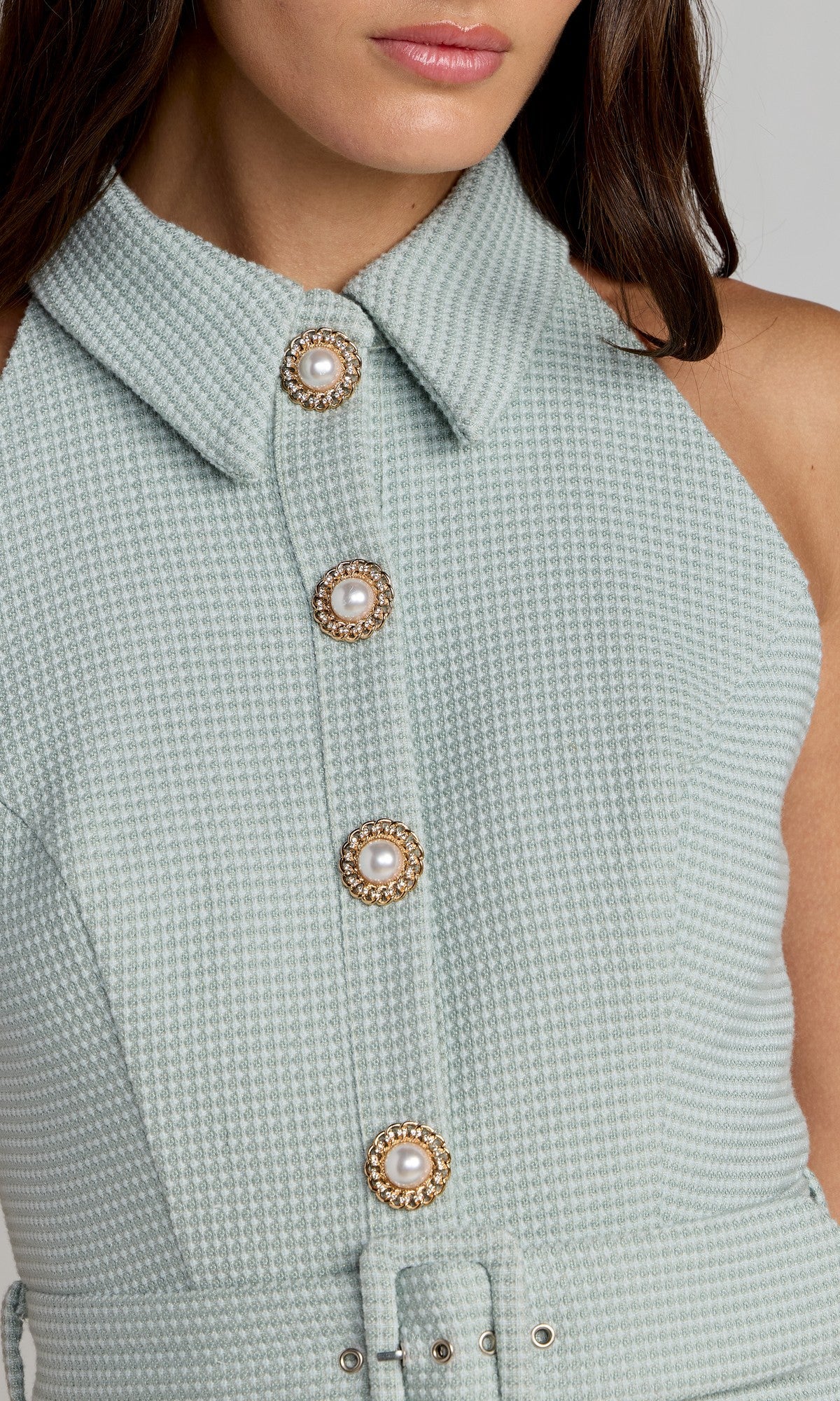 Close-up of a woman wearing the Mac Duggal 27766 Short Party Dress, a light blue textured sleeveless collared design featuring four decorative pearl buttons down the front for a chic look.