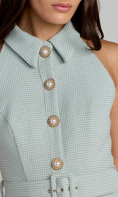 Close-up of a woman wearing the Mac Duggal 27766 Short Party Dress, a light blue textured sleeveless collared design featuring four decorative pearl buttons down the front for a chic look.