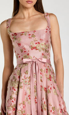 A woman wearing the Midi Party Dress: Mac Duggal 27767—a sleeveless, pink floral midi dress featuring a square neckline and a matching satin bow at the waist, exuding elegant charm.