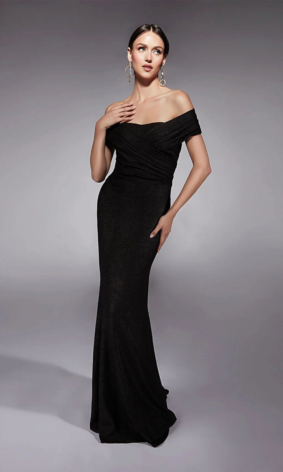 A woman models the Alyce 27767 long formal dress, fitted and off-the-shoulder, paired with statement earrings against a plain gray background.