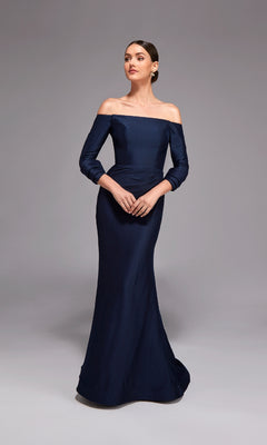 A woman poses against a plain gray background wearing the Long Formal Dress: Alyce 27782, a navy blue off-shoulder mermaid gown.