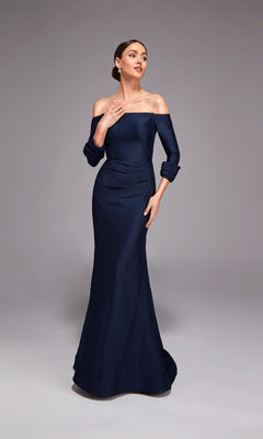 A woman models the Alyce 27782 long formal dress—navy blue, off-shoulder mermaid style in stretch mikado with long sleeves and a floor-length silhouette—posing elegantly against a plain grey background.