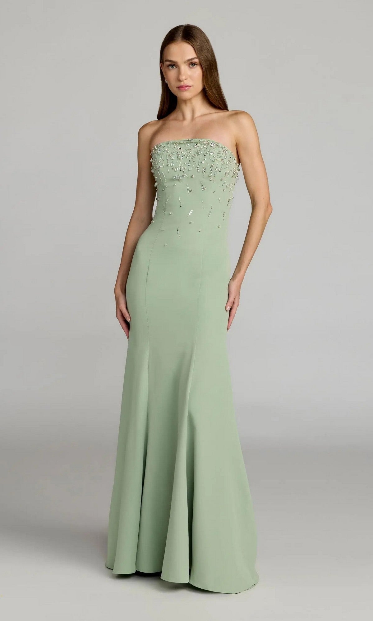 A woman stands against a plain background wearing the Mac Duggal 27788 long formal dress in sage, featuring a strapless design, decorative rhinestone embellishments on the bodice, and a graceful mermaid silhouette.