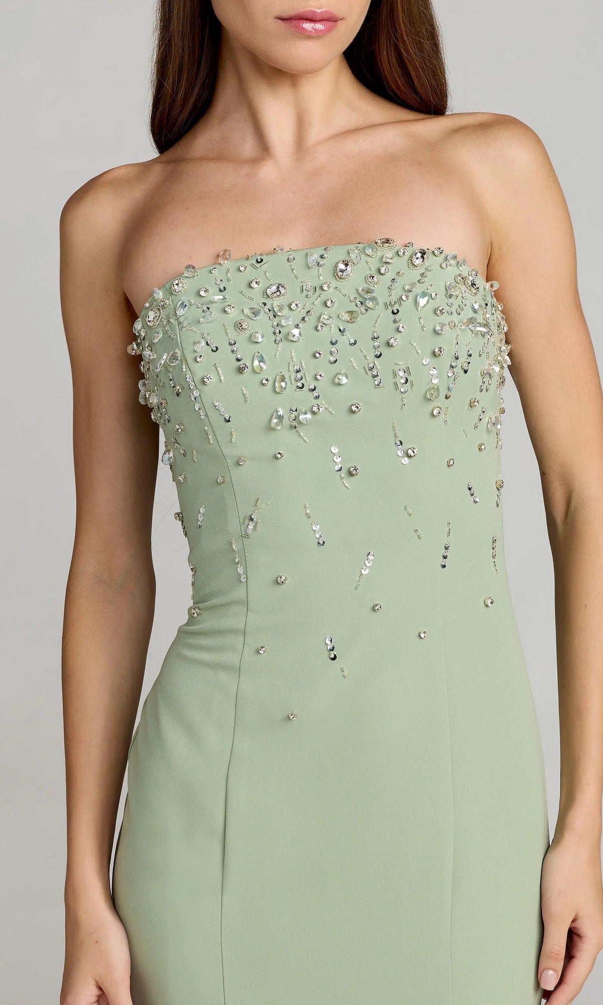 A woman is wearing the Mac Duggal 27788 long formal dress, featuring a strapless sage-green design with a fitted mermaid silhouette and scattered rhinestone embellishments on the bodice.