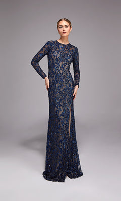 A woman poses against a plain grey background wearing the Alyce 27788 Long Formal Dress in Navy/Sand—a beaded, floor-length gown with long sleeves and a high slit.