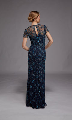 A woman stands facing away in the Alyce 27789 long formal dress, a navy blue gown with short sleeves, detailed floral beading, and her hair styled in a low bun.