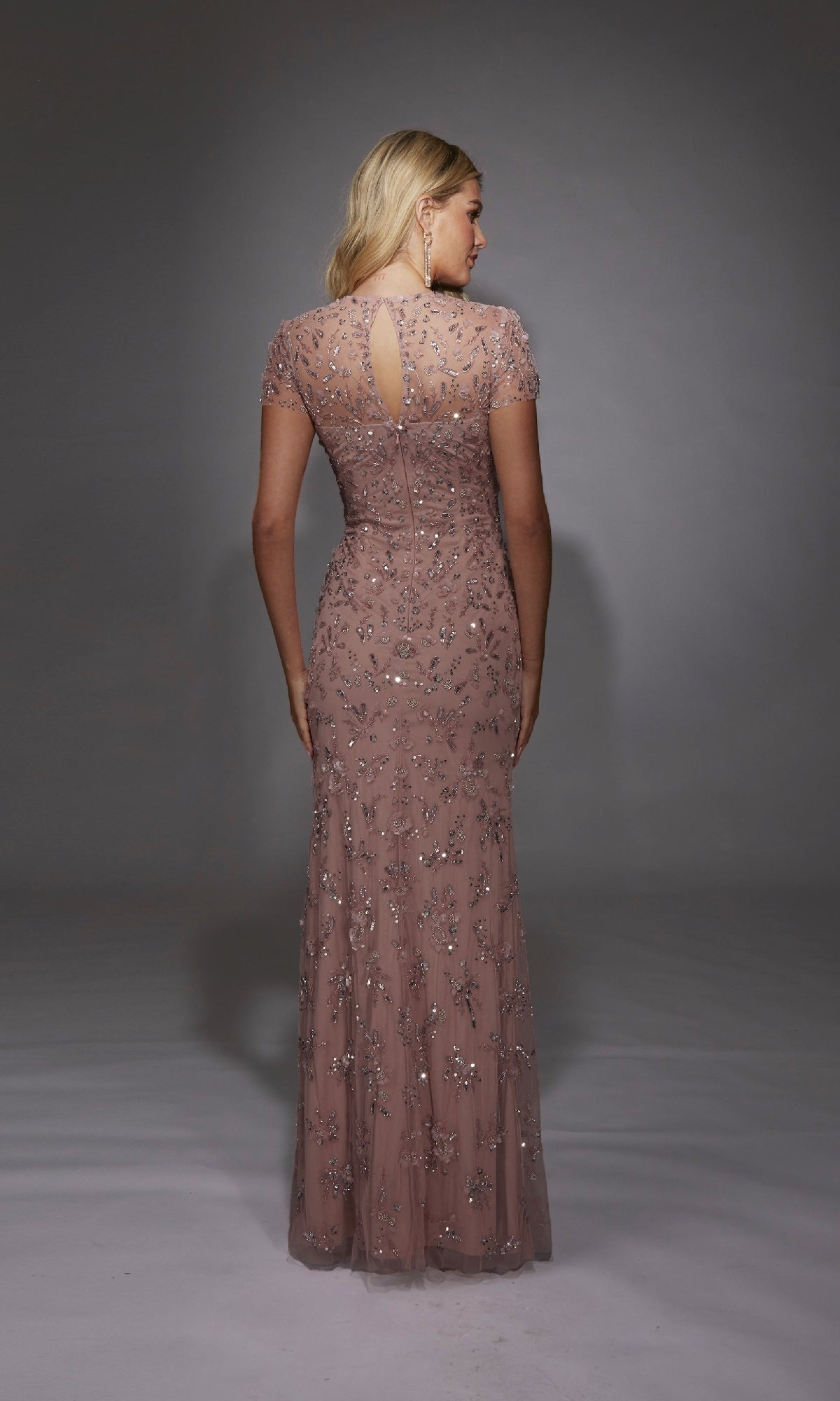 A woman faces away in the Alyce 27789 long formal dress, featuring mauve sequin embellishments, short sleeves, and a keyhole back, set against a plain studio backdrop.