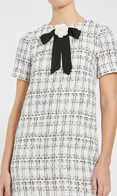 A woman wearing the Mac Duggal 27796 short semi-formal dress, featuring short sleeves, a black-and-white plaid pattern, and chic details like a black ribbon with a white flower accent at the collar—reminiscent of a stylish black bow mini dress.