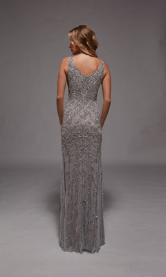 A woman stands facing away in the Alyce 27799, a sleeveless silver gown with intricate beadwork and a V-back—an elegant long formal dress ideal for any special occasion.
