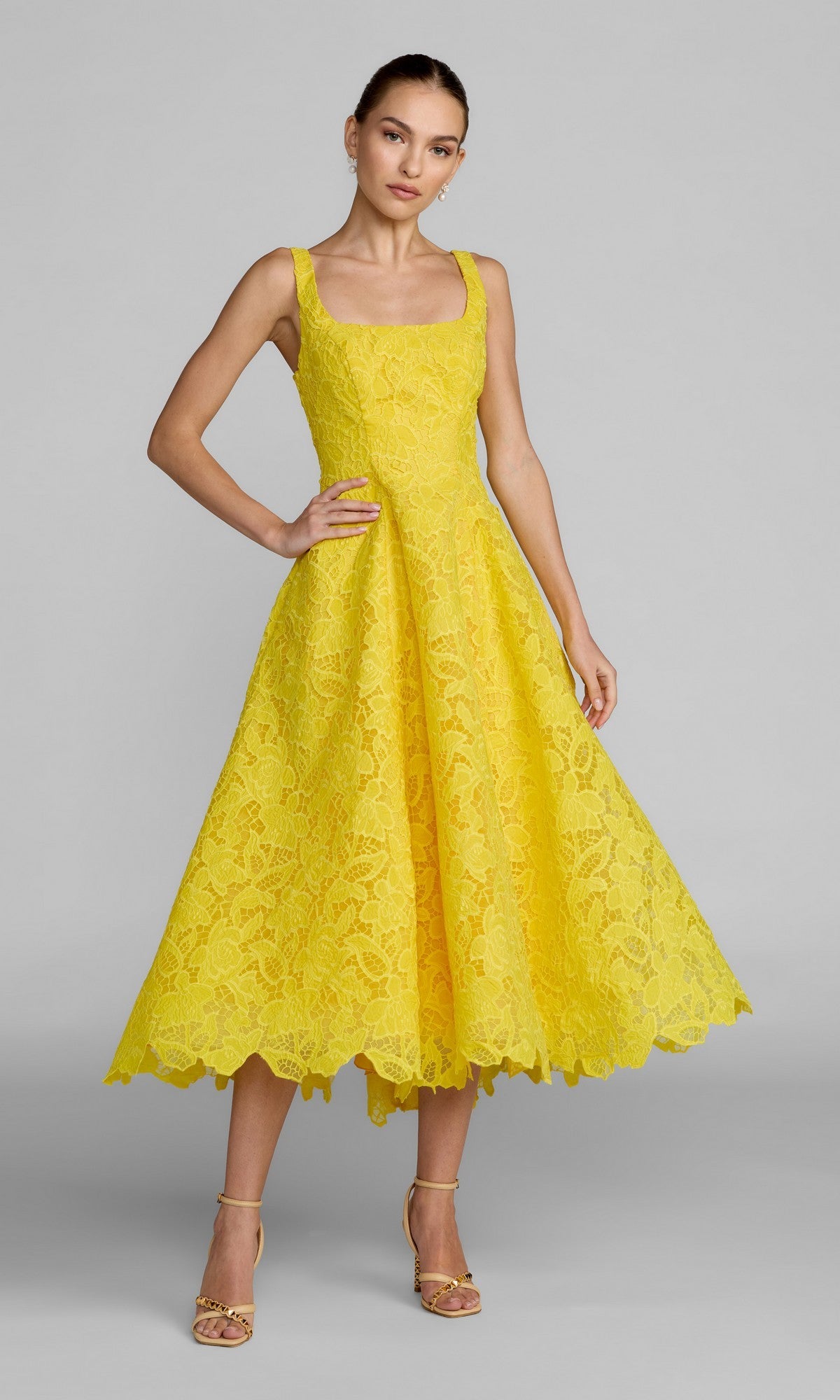 A woman wearing the Mac Duggal 27801 tea-length party dress in buttercup, featuring a sleeveless design, square neckline, and flared skirt, stands in heels against a plain gray background.