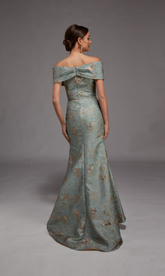 A woman faces away, wearing the Alyce 27802 Long Formal Dress—an off-the-shoulder, floor-length gown with a fitted bodice and metallic floral pattern—set against a plain gray background.