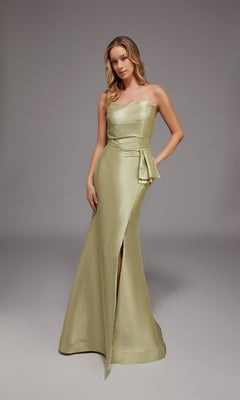A woman poses in a studio wearing the Alyce 27806 long formal dress in honeydew, featuring a one-shoulder design, side slit, and waist sash.