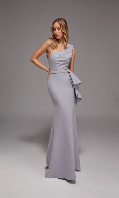 A woman in an Icelandic Blue Alyce 27812 long formal dress featuring a one-shoulder neckline and crystal beaded accent stands against a plain gray background.