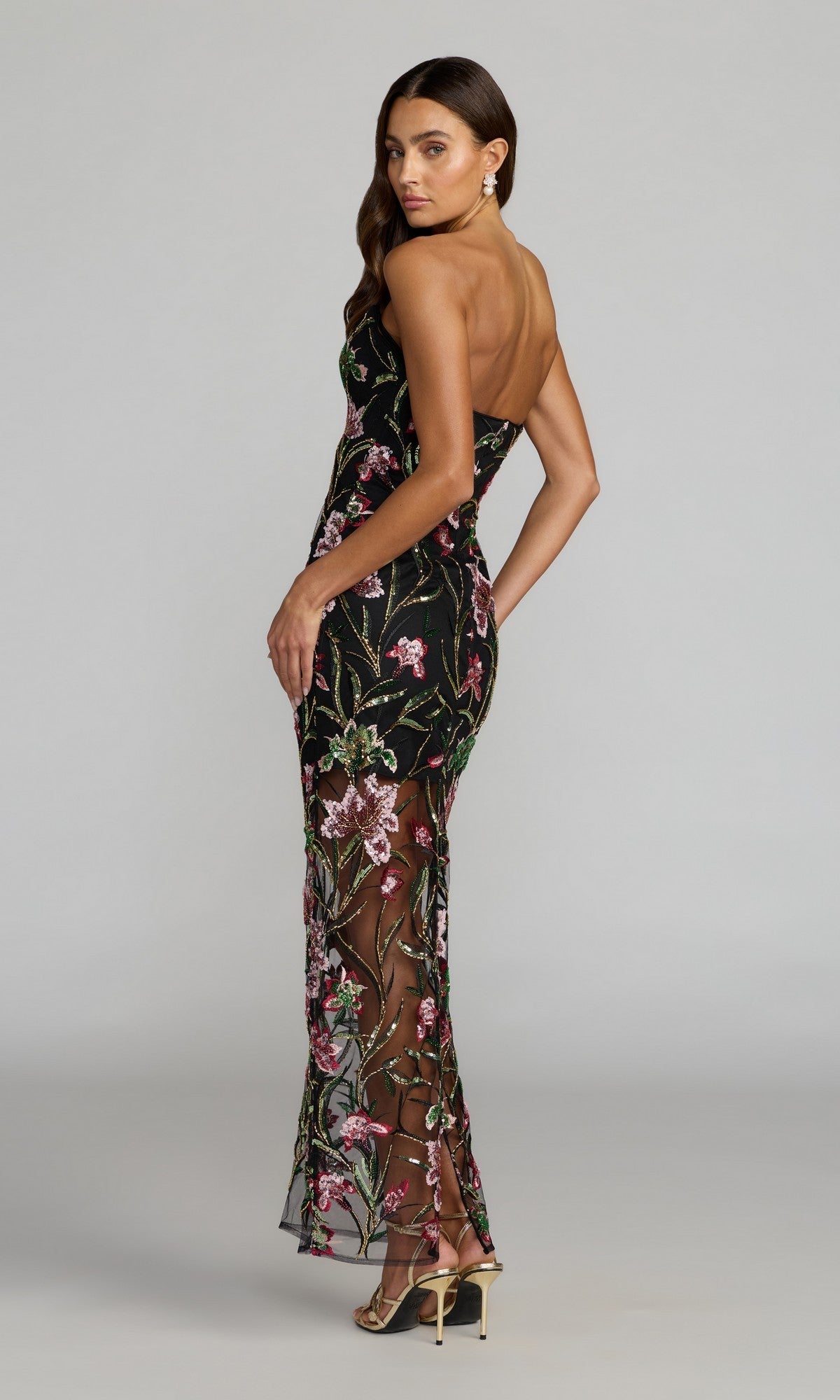 A woman poses in a studio wearing the Mac Duggal 27814, a long formal strapless black gown featuring colorful floral embroidery and sheer panels.