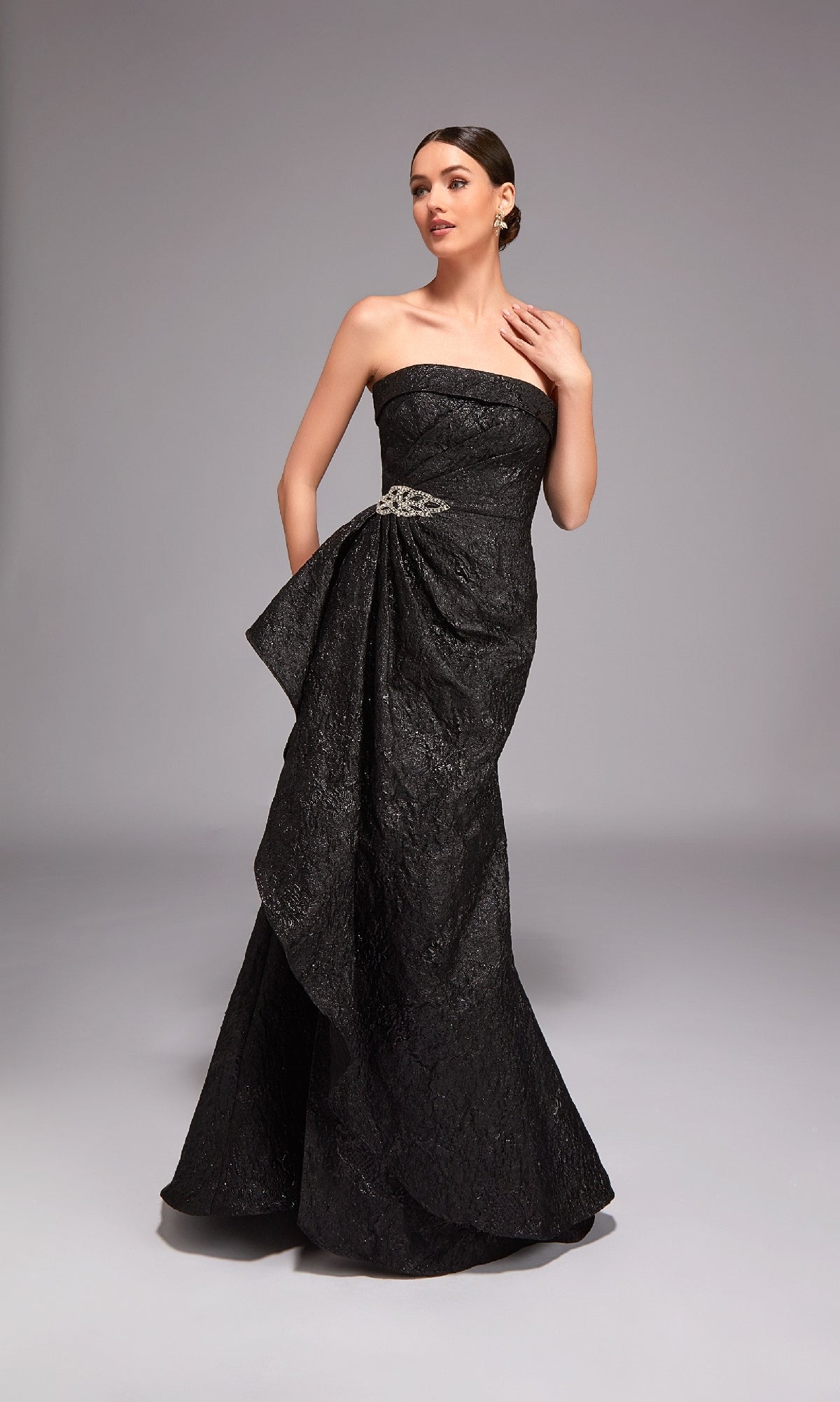 A woman poses elegantly in the Alyce 27818 Long Formal Dress, a strapless jacquard gown featuring textured details and side embellishment—an ideal choice for special occasions, photographed against a plain studio backdrop.