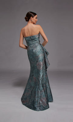 A woman models the Alyce 27818 Long Formal Dress—a strapless jacquard gown with a metallic textured finish, floor-length skirt, and side ruffle—posing with her back to the camera against a plain background.