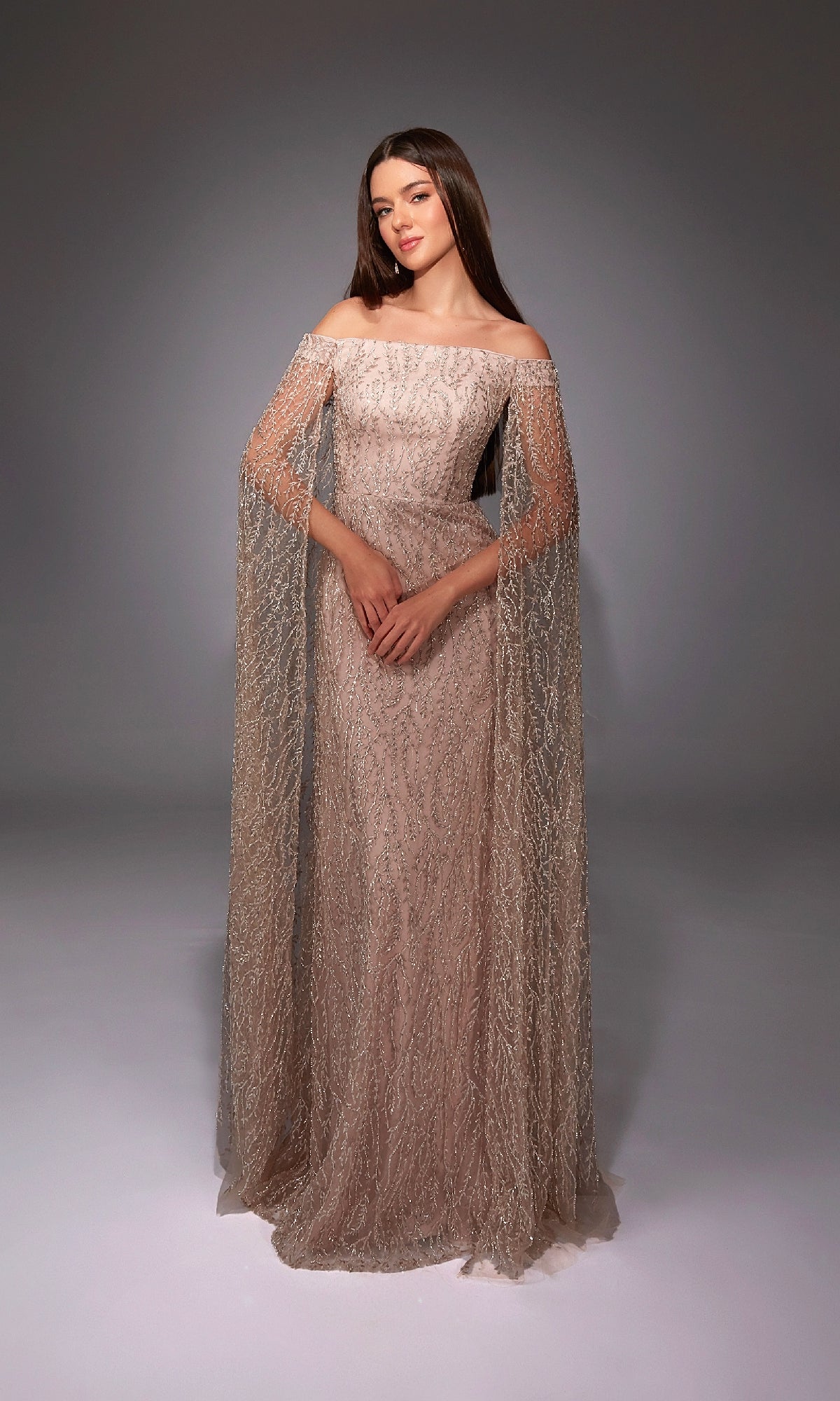 A woman poses in the Alyce 27821 long formal dress featuring a fitted silhouette, off-the-shoulder straps, sheer embellished sleeves, and a floor-length hem against a plain studio backdrop.