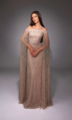 A woman poses in the Alyce 27821 long formal dress featuring a fitted silhouette, off-the-shoulder straps, sheer embellished sleeves, and a floor-length hem against a plain studio backdrop.