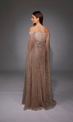 A woman faces away in the Alyce 27821 long formal dress, showcasing off-the-shoulder straps, shimmering sheer fabric, and a subtle train against a plain gray background.