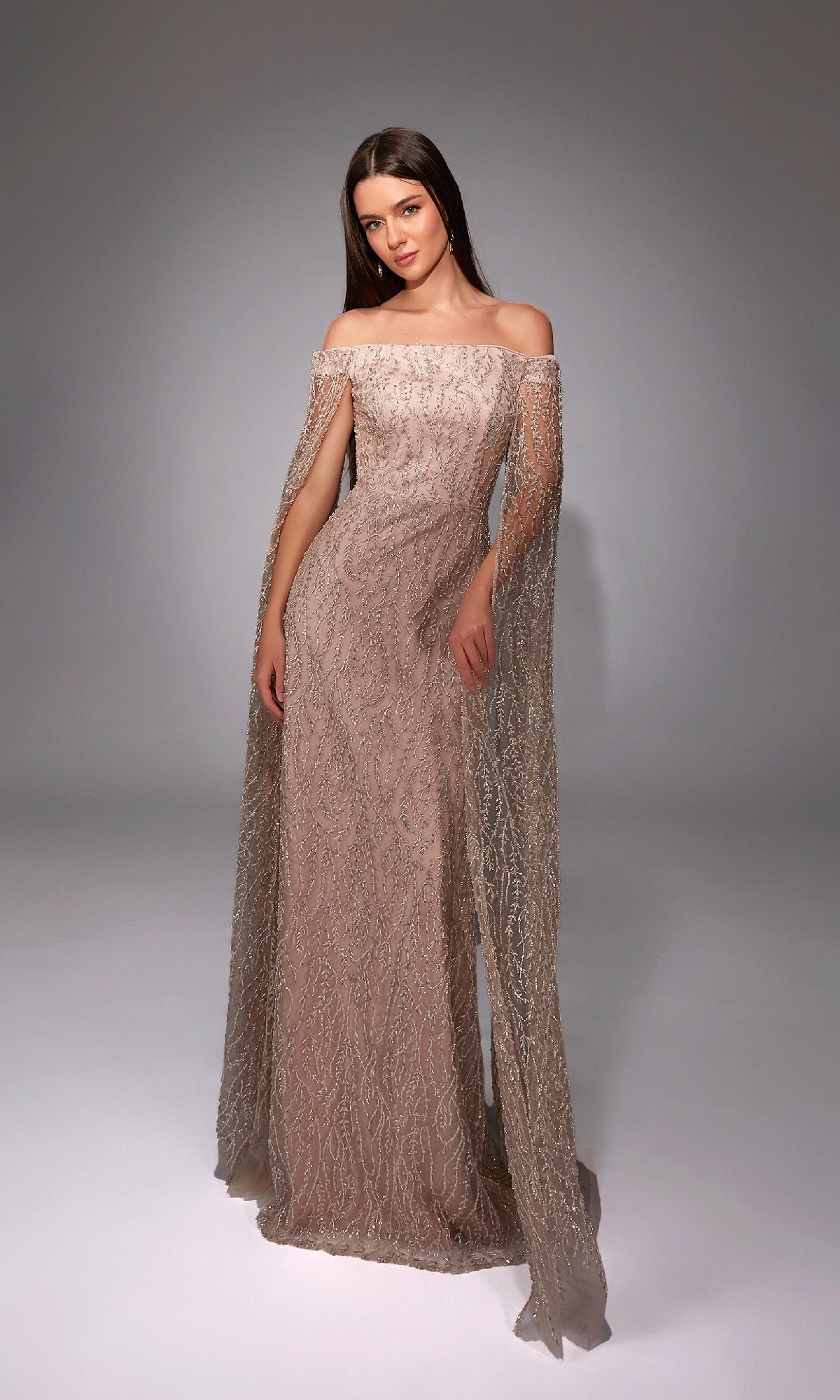A woman poses in a studio wearing the Alyce 27821 long formal dress, which features off-the-shoulder straps, sheer draped sleeves, and intricate beading.