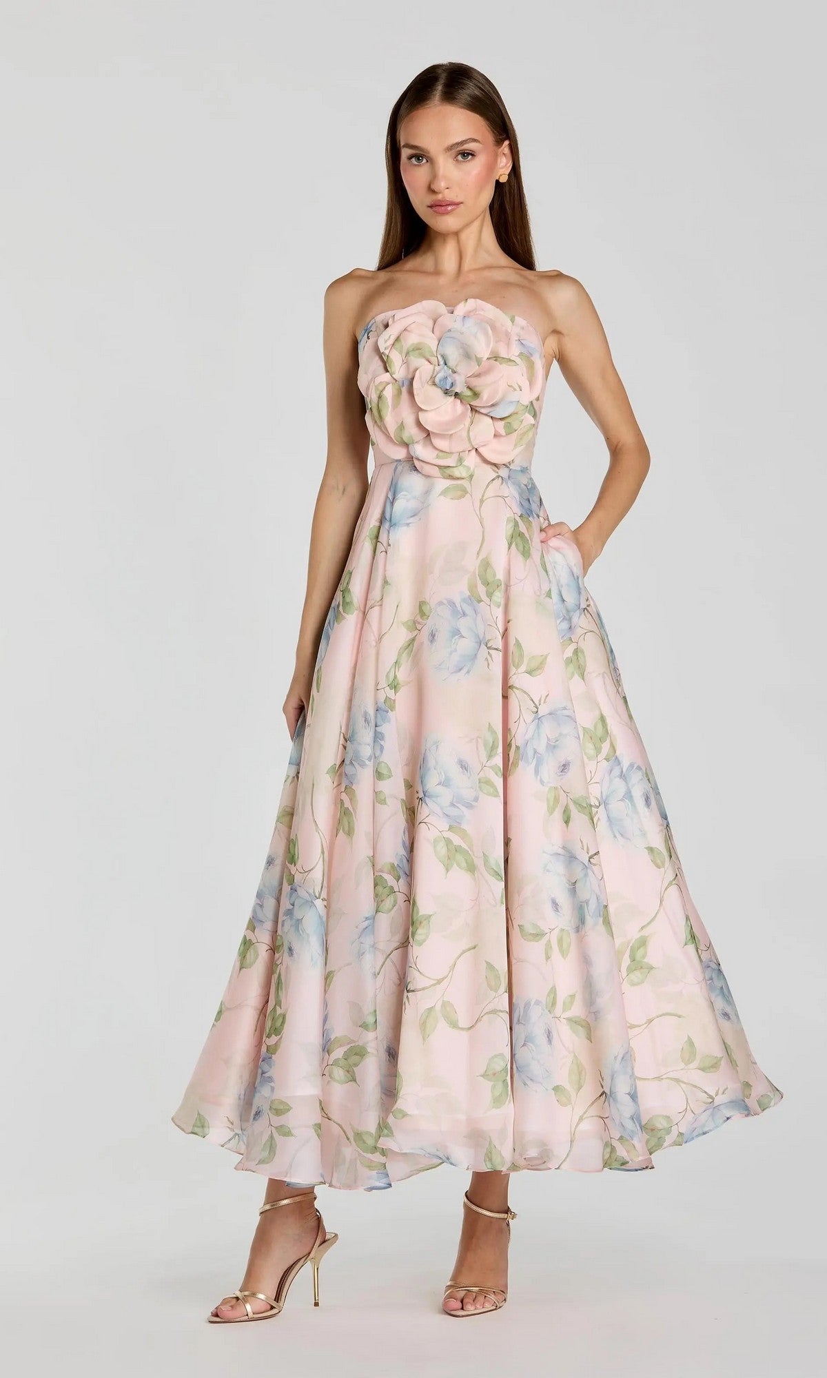 A woman wears the Mac Duggal 27822 Midi Party Dress, a floral organza midi dress with a 3D flower bodice in pastel pink and blue, standing against a plain background.