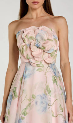 A woman wearing the Midi Party Dress: Mac Duggal 27822—a strapless, pastel pink organza midi dress featuring blue floral print and a striking large 3D flower detail on the bodice.