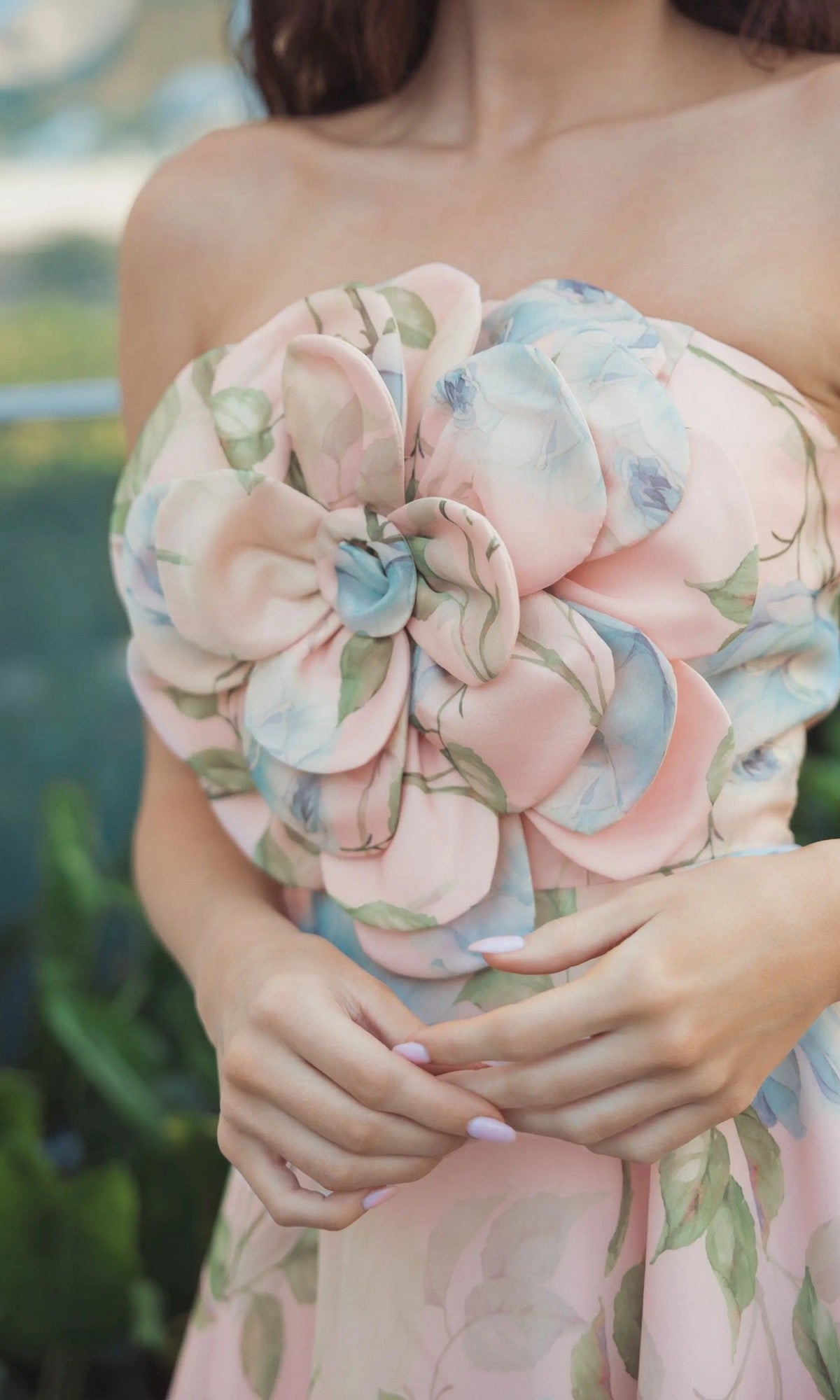 A woman stands outdoors with her hands clasped, wearing the Mac Duggal 27822 Midi Party Dress—a strapless, pastel floral organza piece featuring a prominent 3D flower detail on the bodice.