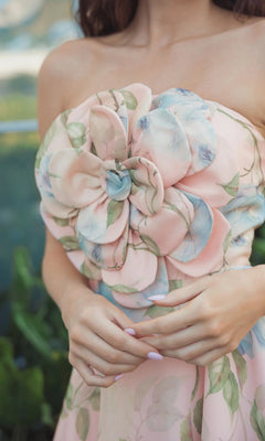 A woman stands outdoors with her hands clasped, wearing the Mac Duggal 27822 Midi Party Dress—a strapless, pastel floral organza piece featuring a prominent 3D flower detail on the bodice.