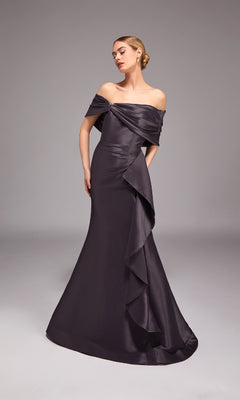 A woman stands against a plain gray background wearing the Alyce 27822 long formal dress in charcoal, featuring an off-the-shoulder neckline, floor-length mermaid silhouette, and ruffled details.