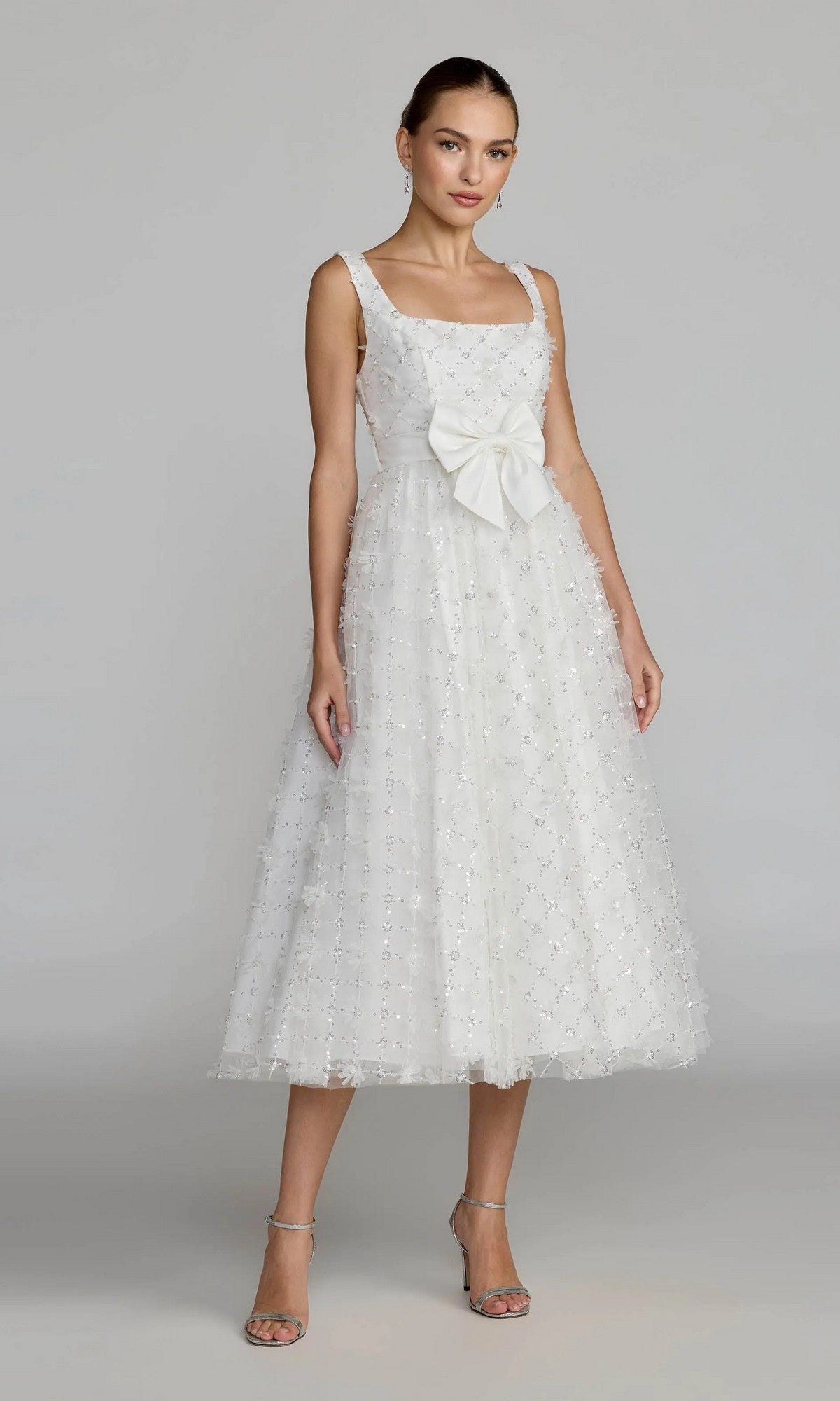 A woman wearing the Mac Duggal 27824 midi party dress in ivory, a sleeveless design featuring a large bow at the waist, stands against a plain gray background.