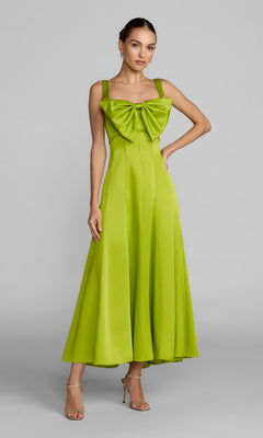 A woman stands in strappy heels against a plain gray background, wearing the Mac Duggal 27826 Midi Party Dress in apple green, which features an A-line silhouette and a large bow on the chest.