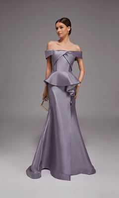 A woman in the Alyce 27827 long formal dress, lilac grey, with an off-the-shoulder peplum design, holds a small clutch while standing against a plain gray background.